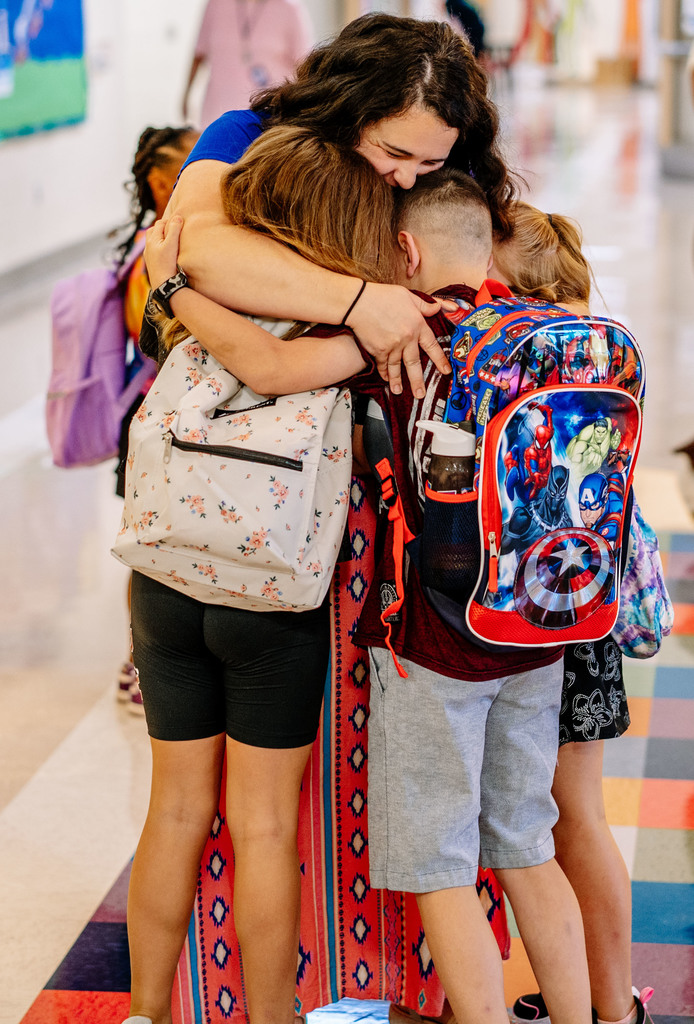 teacher hugging students as they walk into school on the first day.