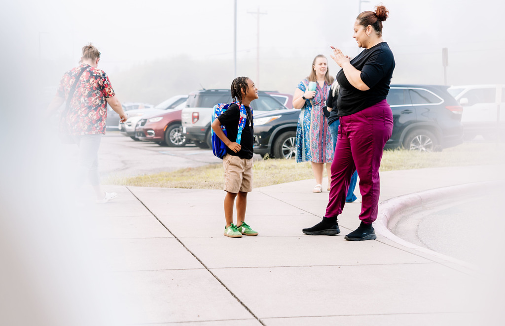 a young boy posing for a picture for his mom before walking into school. 