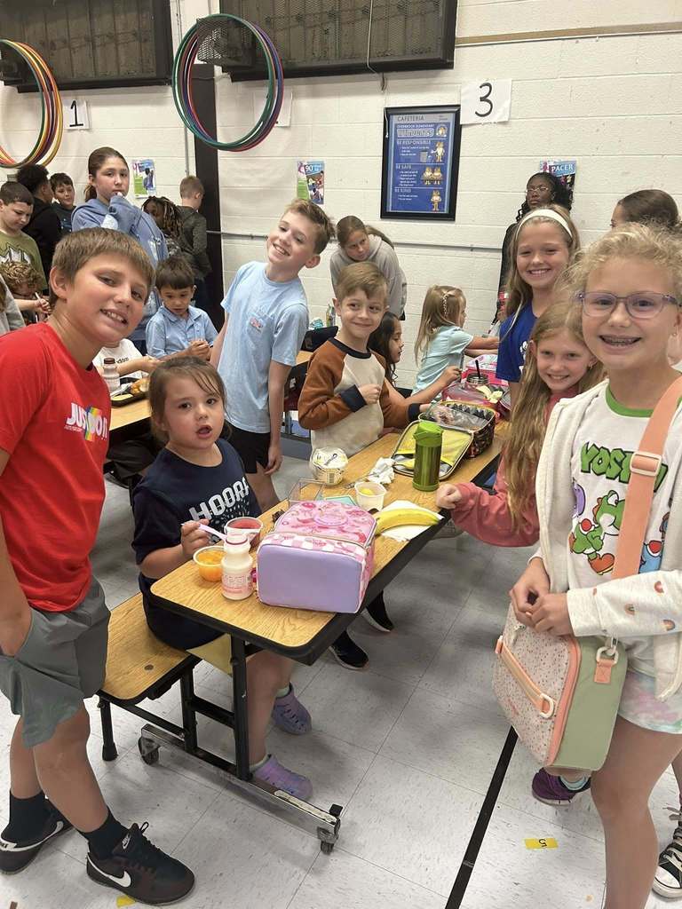 5th grade and kindergarten students at overbrook elementary smile for a picture in the lunch room.