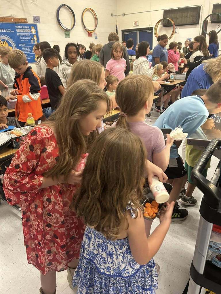 a 5th grade student is helping a kindergarten student with her lunch tray.