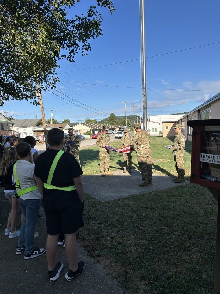 nhs rotc students folding the american flag while nes 5th grade students watch.