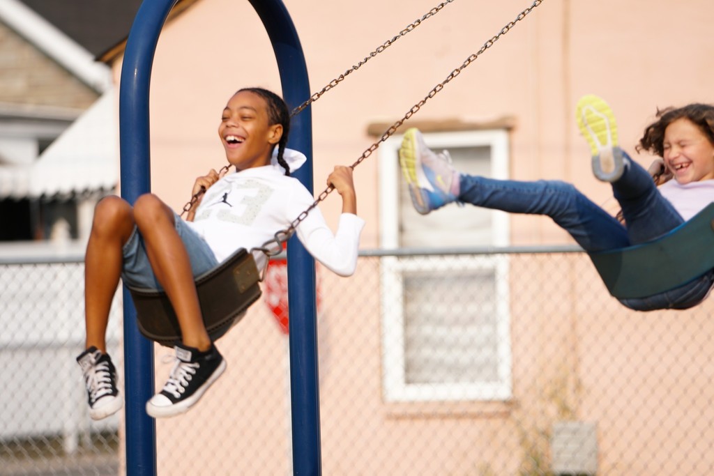 two belle elementary students laughing while they swing on the playground at school.