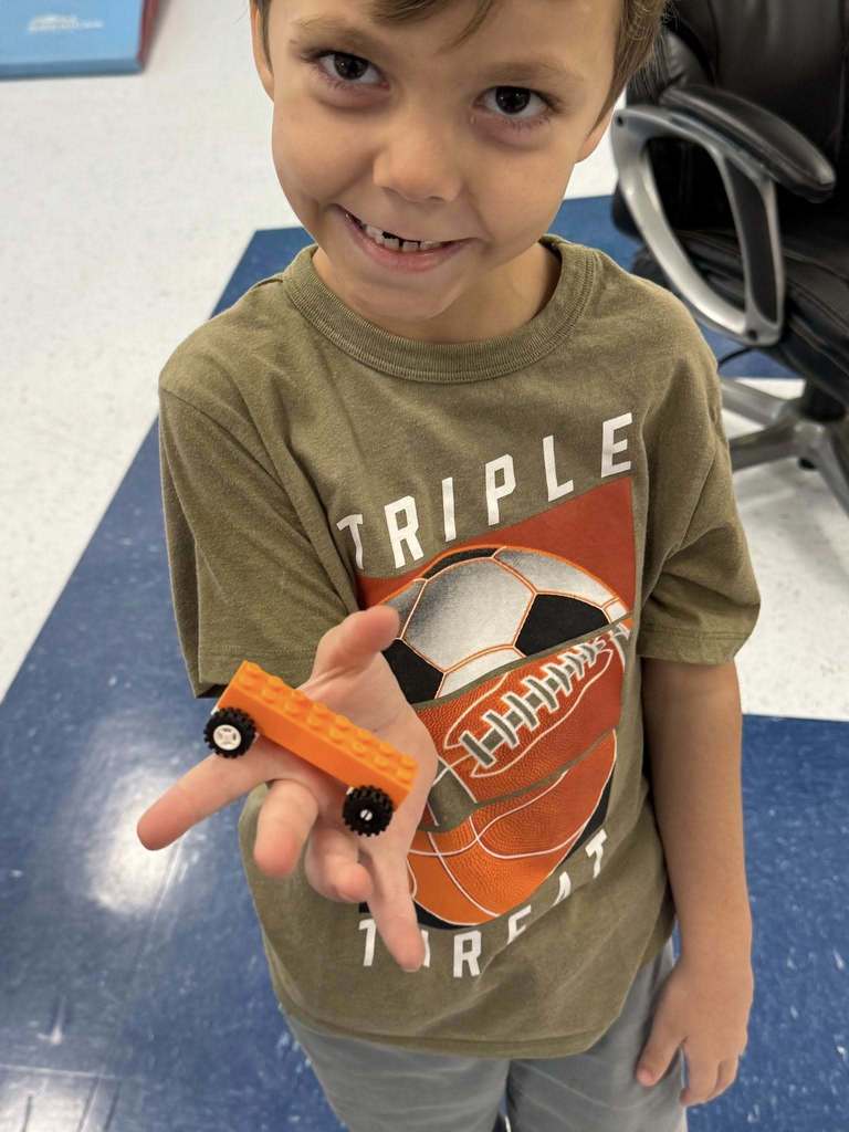 student showing off his orange lego car. 