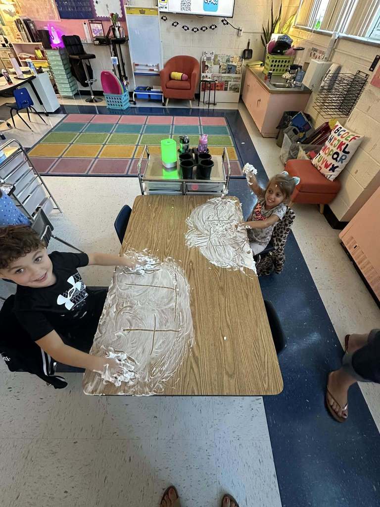 two bridgeview elementary students writing their names in shaving cream during a handwriting lesson.