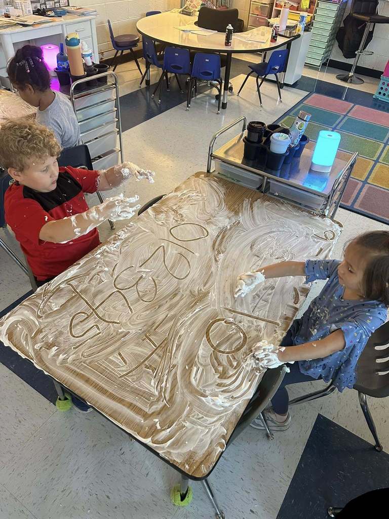 two bridgeview elementary students writing their names in shaving cream during a handwriting lesson.