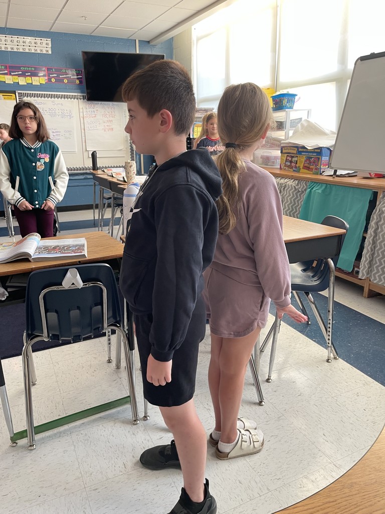 students standing back to back listening to the discussion prompt from their teacher.