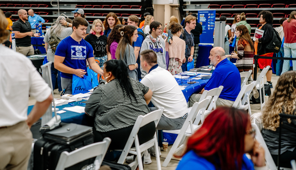 high school juniors and seniors walking around the gymnasium at the university of charleston speaking with representatives from universities. 