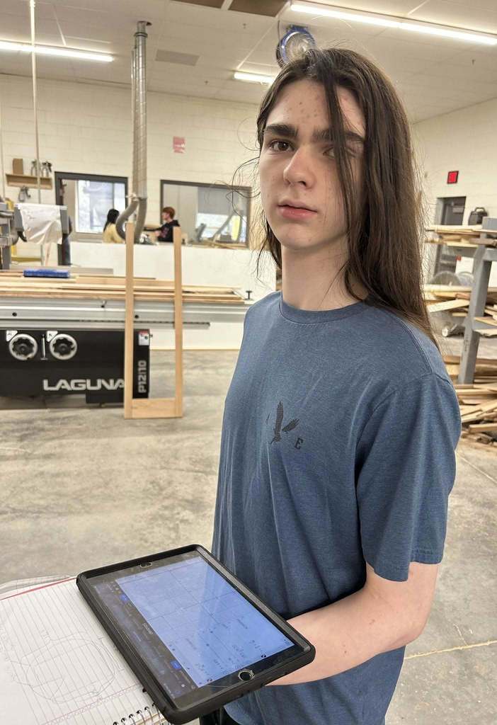 student in the wood shop solving a math problem in his notebook.