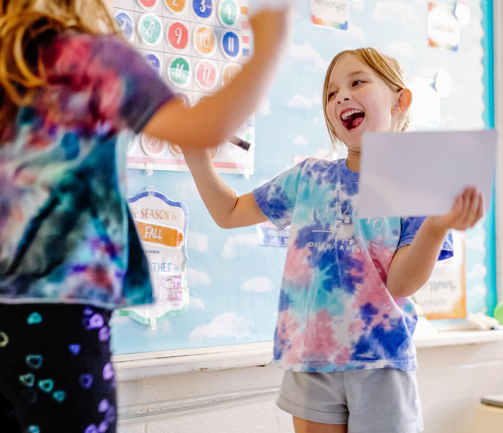 two kindergarten students celebrate together after getting the correct answer during a classroom lesson.