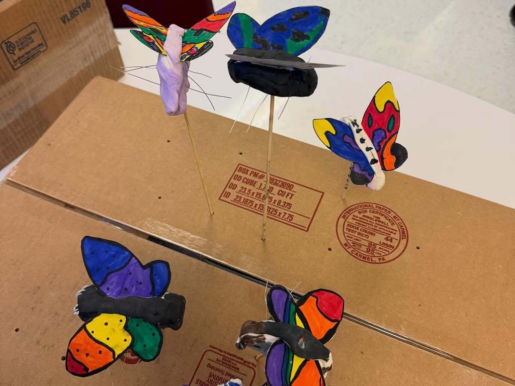 3D butterflies made by students attached to a box with a wooden dowels.