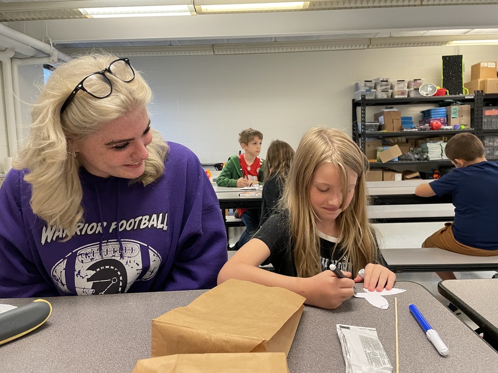 a riverside high school student looking on as an elementary student colors part of her butterfly black. 