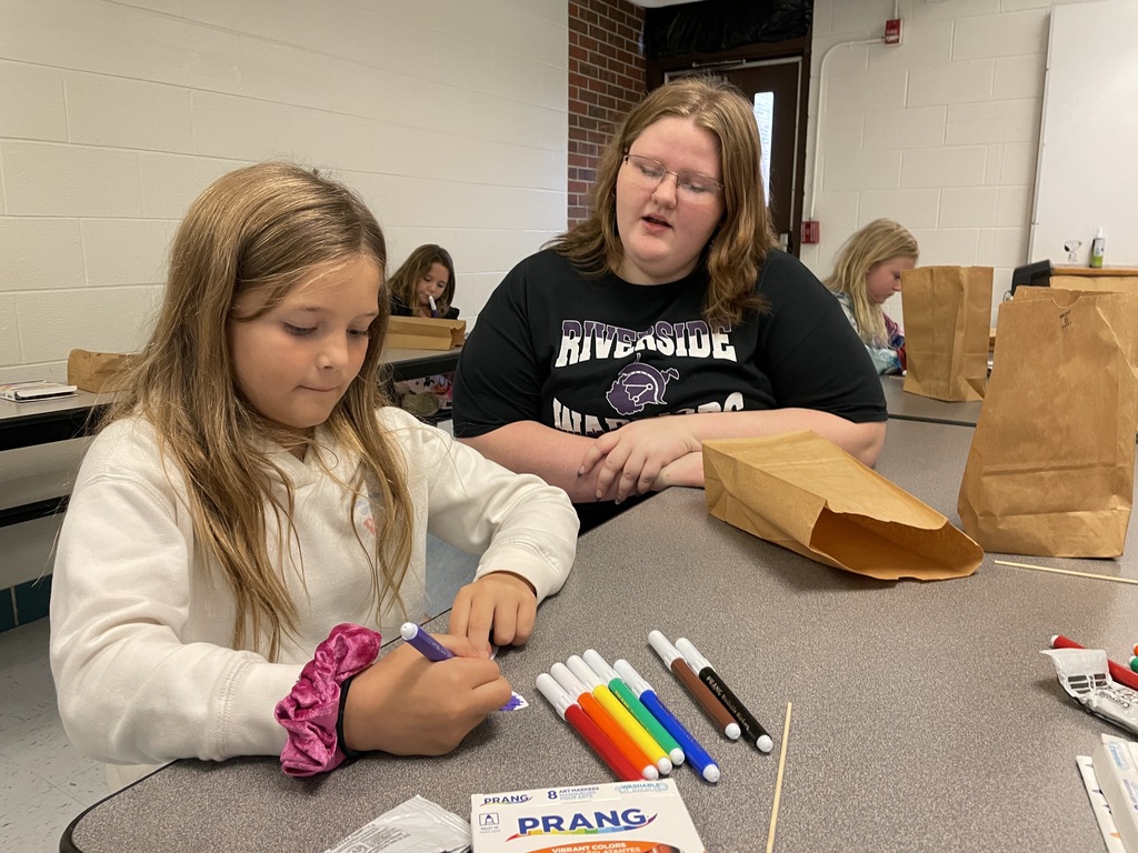 a riverside high school student looking on as an elementary student colors part of her butterfly purple. 