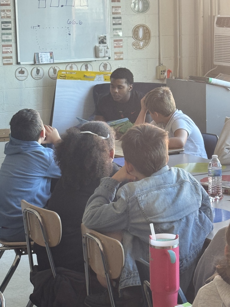 a south charleston high school football player seated in the front of an elementary classroom reading to students. 