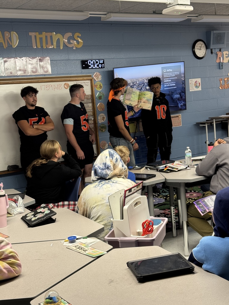 four south charleston high school football players standing in front of an elementary classroom reading to students.
