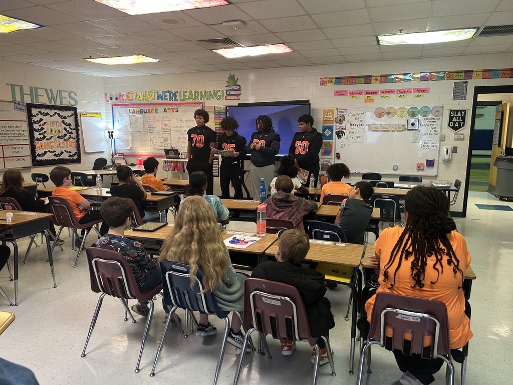 four south charleston high school football players standing in front of an elementary classroom reading to students.