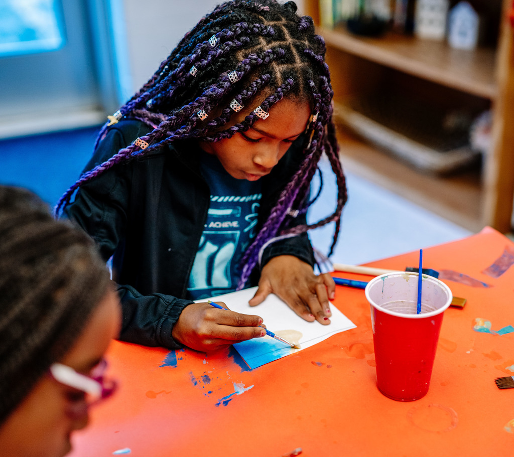 a girl painting on her paper with the color blue.