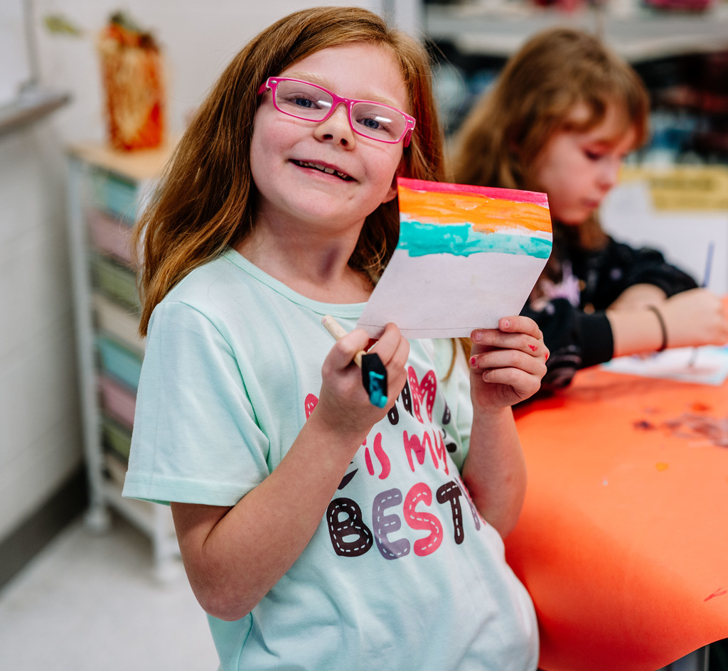 a student holding up her painting and smiling.