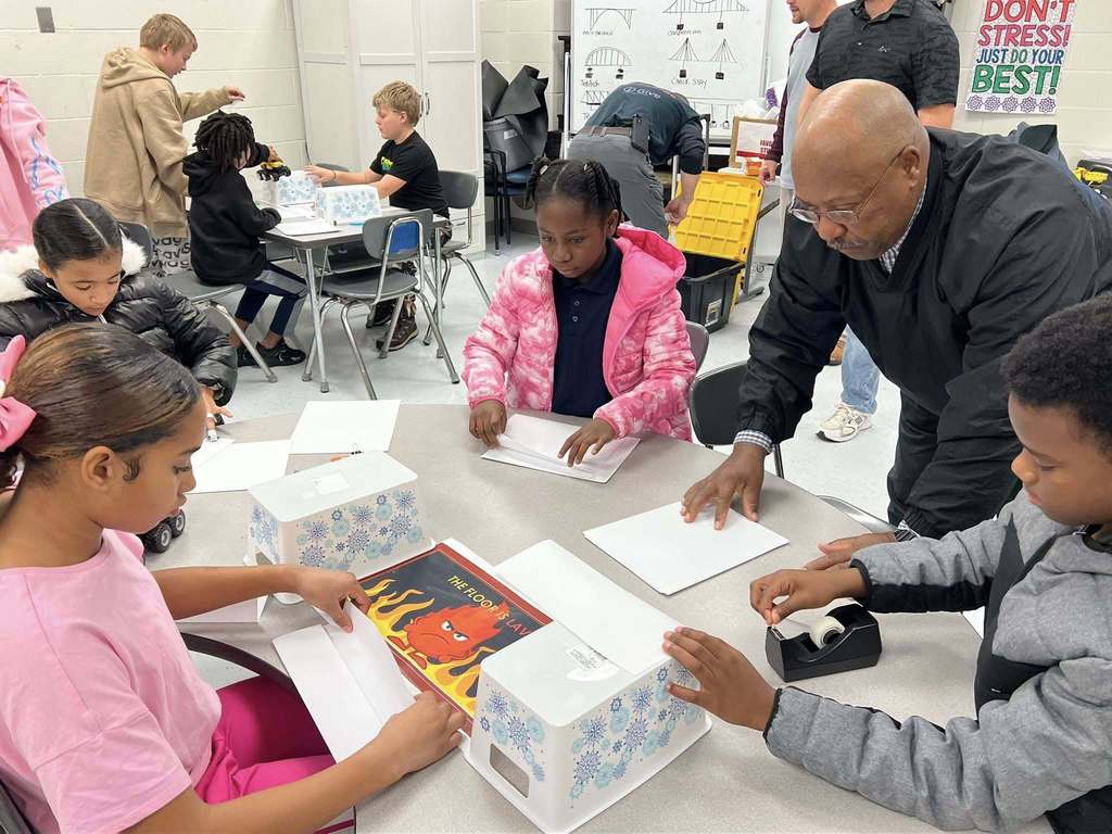 a teacher working with a group of students as they begin to build their bridge.