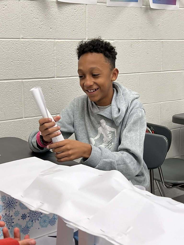 a student laughing while putting together a pillar for his bridge.