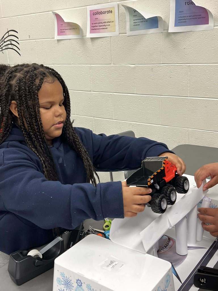 a student placing a toy car on top of her group's bridge to test the strength of the bridge.