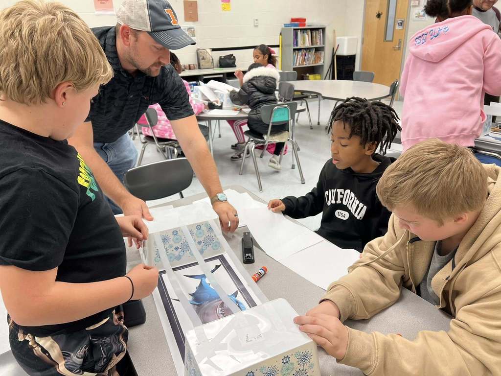 a teacher working with a group of students as they begin to build their bridge.