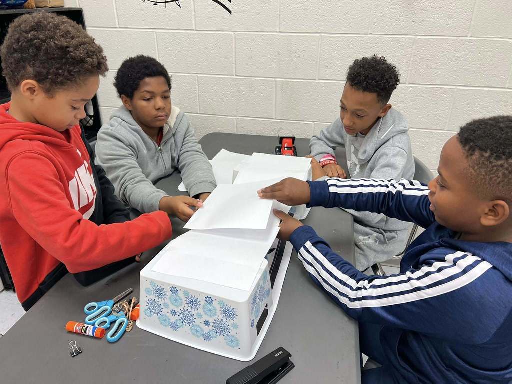 four students testing different methods to make their bridge strong.