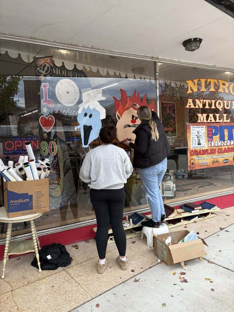 nitro high school art students painting a window display at the nitro antique mall.
