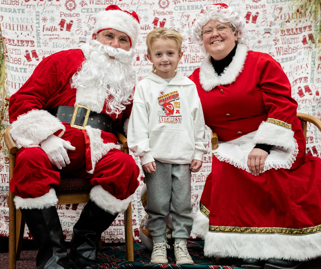 A student standing in between santa claus and mrs. claus.