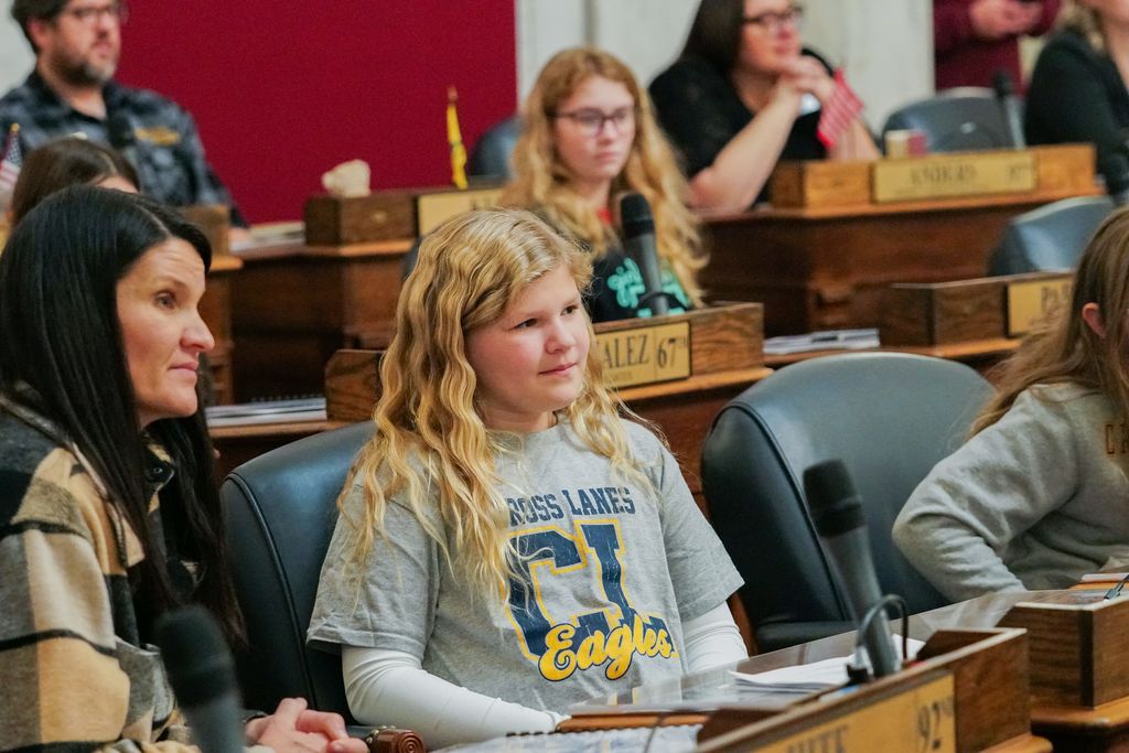 a young student listening to a presenter inside of the west virginia house of delegates chamber.