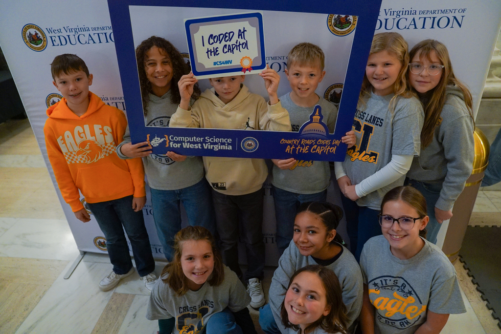 students posing for a picture in front of a wvde backdrop and holding up a sign that says I coded at the capitol.
