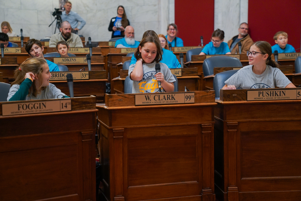 a student speaking in the west virginia house of delegates while standing behind a delegates desk.