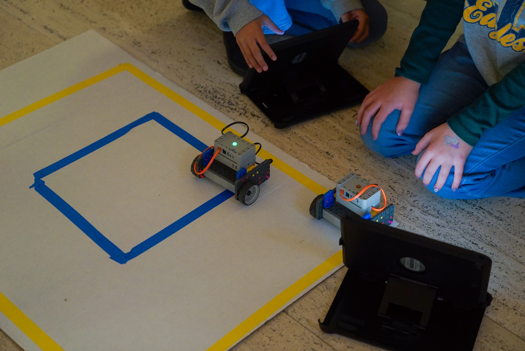 a robot, built by students, is sitting on a mat while students start up the program that makes the robot move.