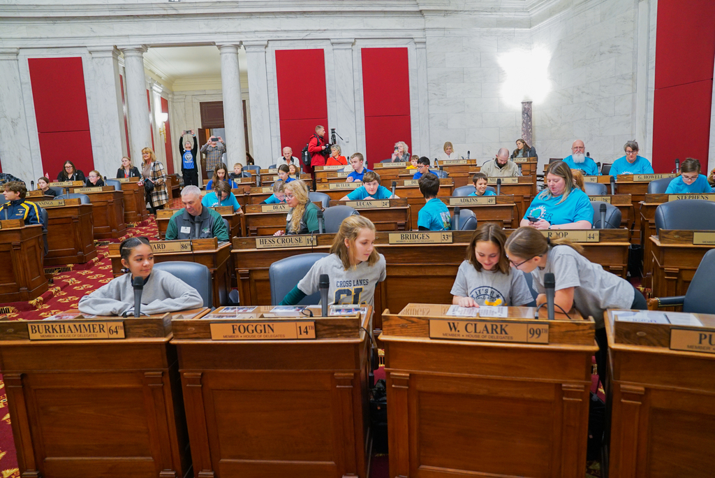 students and their teachers sitting at delegate's desks in the west virginia house of delegates chamber.
