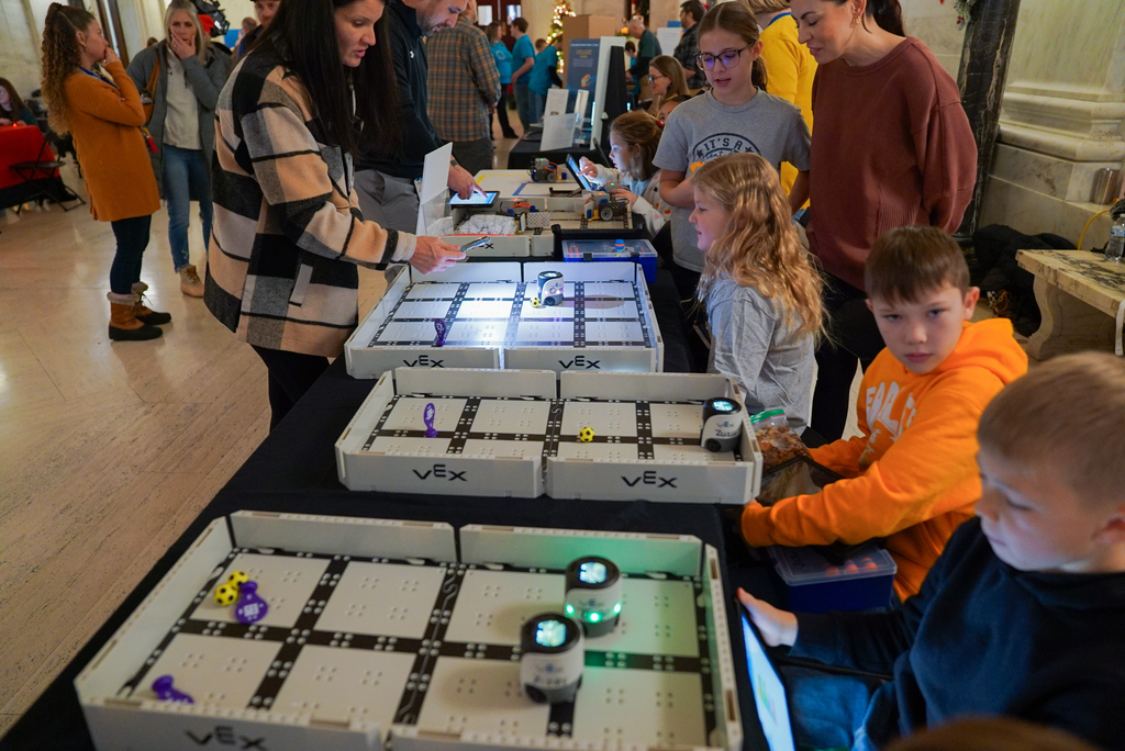students sitting down in front of their robotics playing field showing people how their robots work.