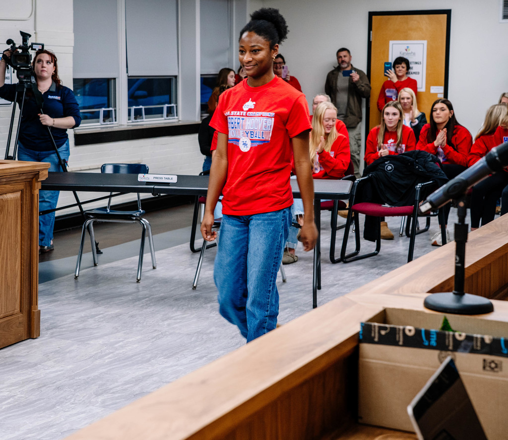 HHHS volleyball player walking up to get her certificate at the kcs board of education meeting and her teammates are clapping in the background.