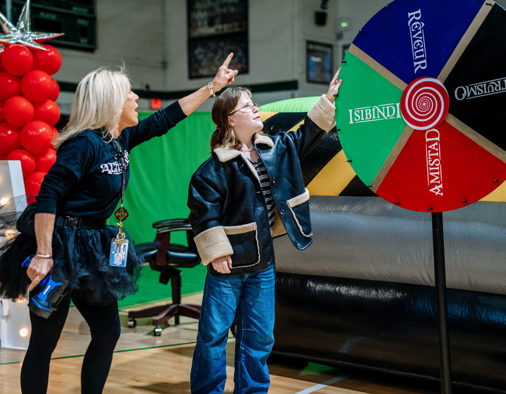 A student is preparing to spin the wheel which will determine which house she belongs to. The school's principal is standing behind the student anxiously waiting for the wheel to be spun.
