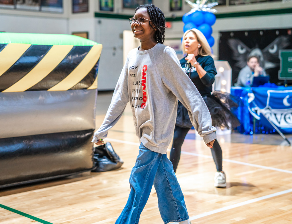 a student anxiously walks towards the house wheel to spin it with the school principal cheering her on.