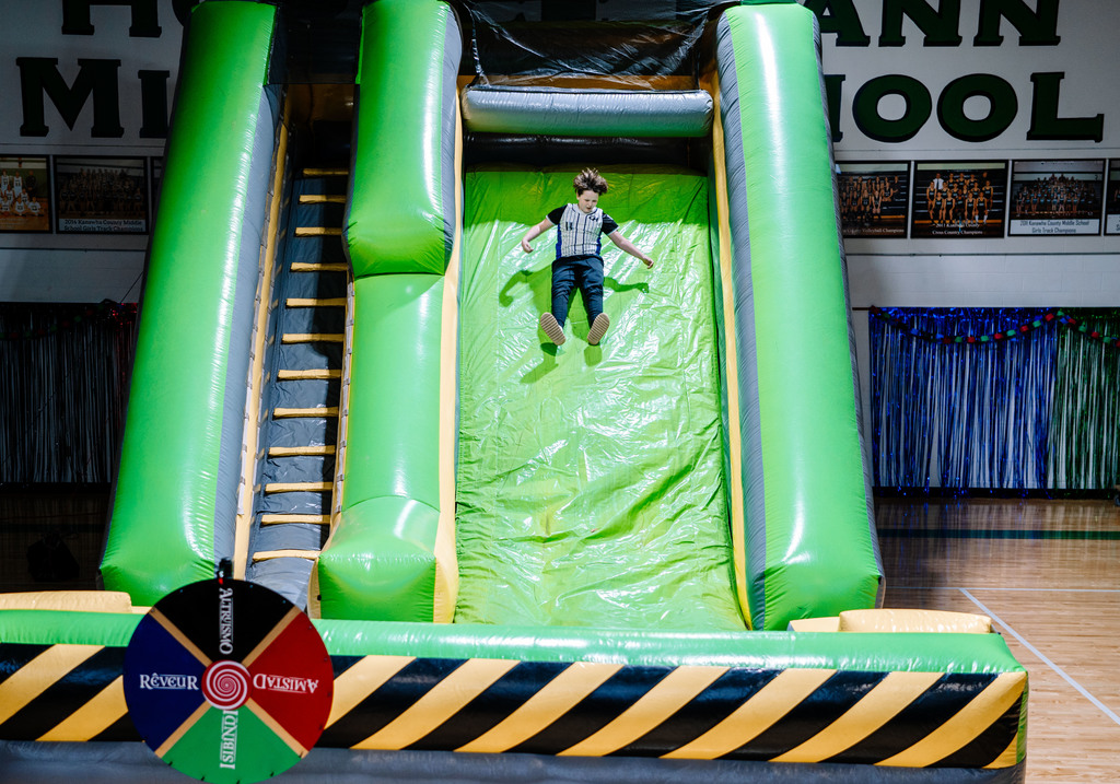 A student is sliding down a giant inflatable slide that is set up in the school gym.