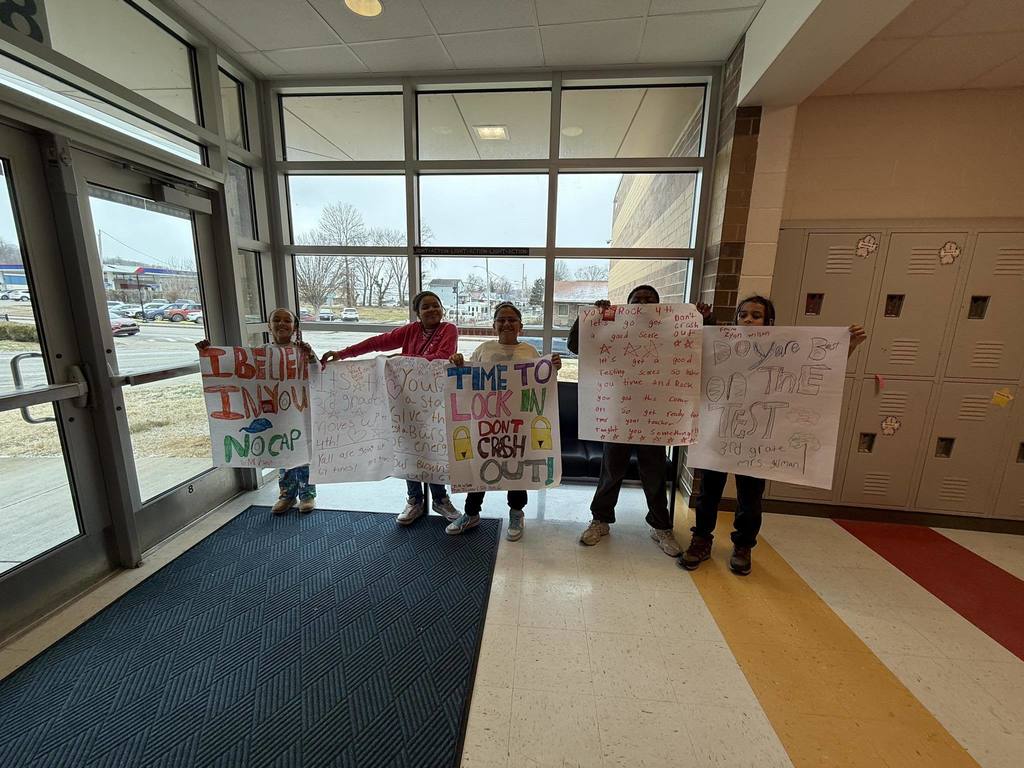 Students at Mary C. Snow West Side Elementary School standing at the entrance of the school holding encouraging signs for students to do well on their upcoming math test.