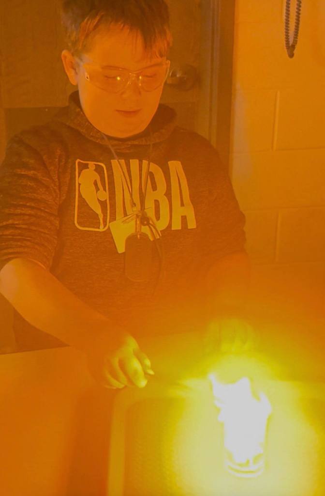 A student is holding an item that can't be seen over a flame.