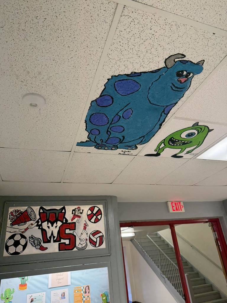 Sully and Mike Wazowski, from the movie Monsters Inc., have been painted on the ceiling at West Side Middle School by art students. Underneath the painting of Sully and Mike, the West Side Middle school logo has been painted on the wall and is surrounded by different sports paintings.