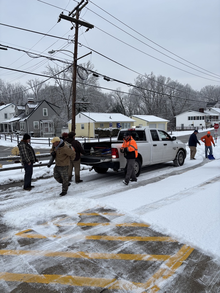 Seven City of South Charleston workers are getting snow removal gear out of a white city truck so they can begin clearing the sidewalk and front entrance at Bridgeview Elementary School in South Charleston.