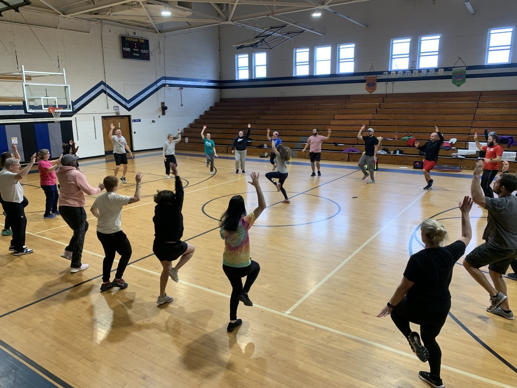 The teachers are in a huge circle in the gym, with one teacher leading the exercise standing at half court.