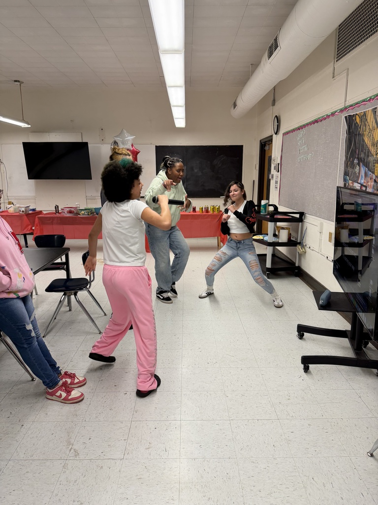 Three girls are doing Karaoke. One student is holding the mic and signing and the other two are dancing.  