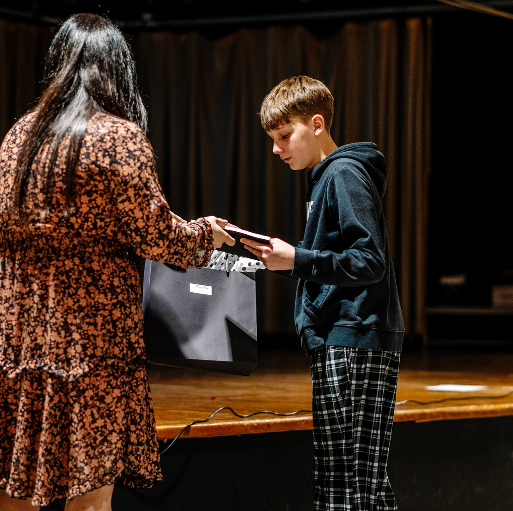 The school principal is handing a student his bag with that has his dress shirt and tie in it. 