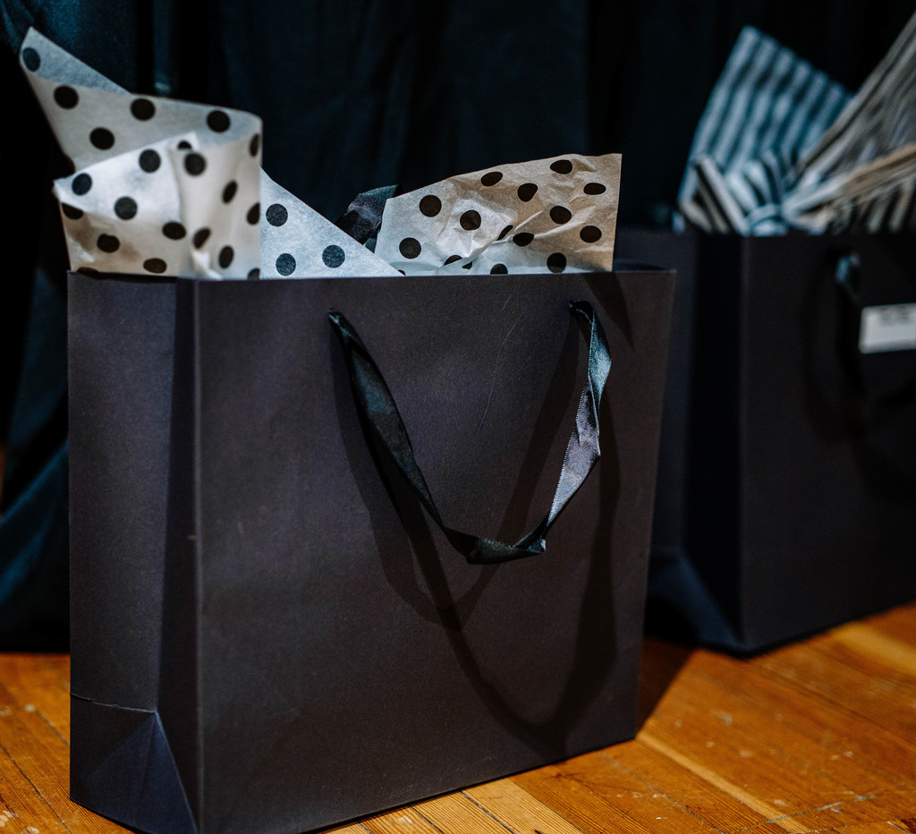 A black gift bag, with white tissue paper that has black polka dots on it, sitting on the DMS auditorium stage. These bags have the student's shirt and tie in them. 