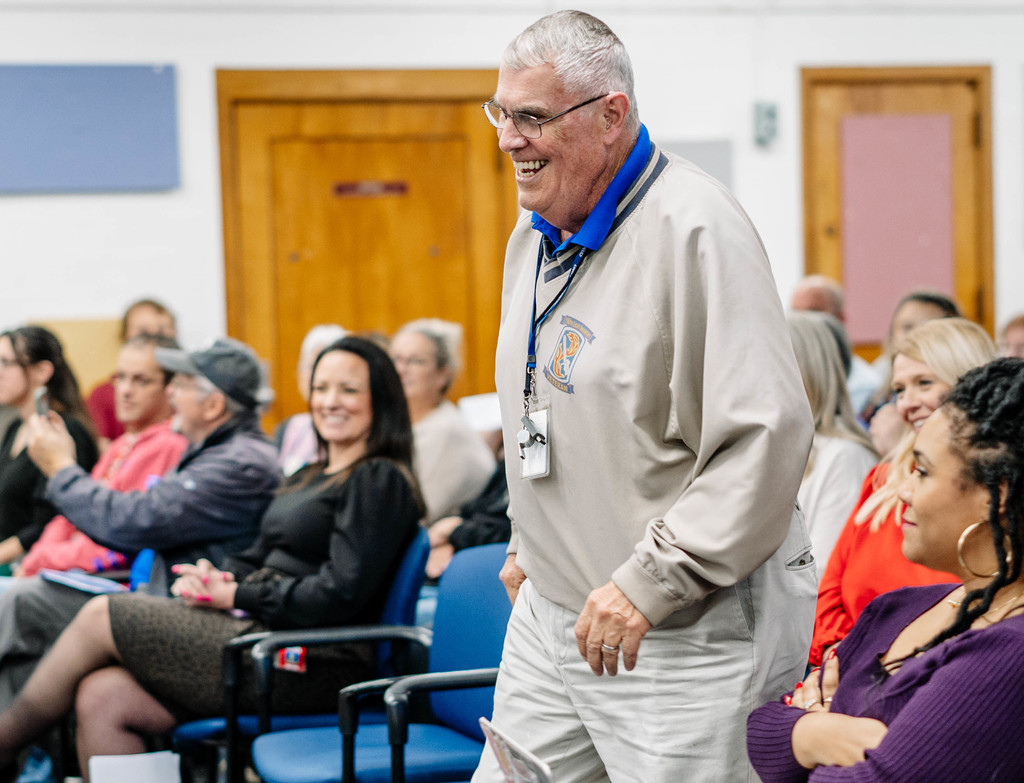 A teacher is walking up the aisle to receive his certificate of recognition.