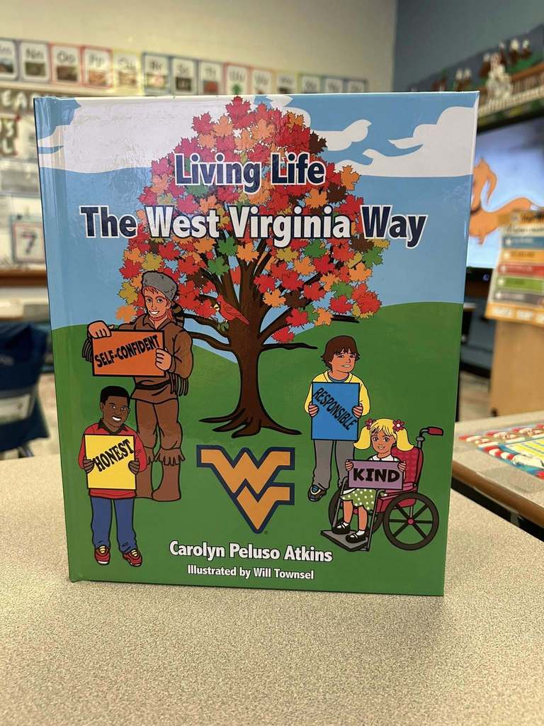 A picture of the book the WVU mascot read to students. The book is called, "Living Life the West Virginia Way" There are four people on the cover of the book holding signs that say self-confident, honest, responsible, and kind. Behind the people is a tree with colorful fall leaves and a Cardinal sitting on a branch. The Flying WV is just below the tree.