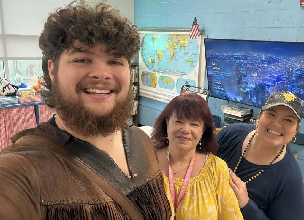 The WVU mascot is taking a selfie with two staff members dress in WVU gear.