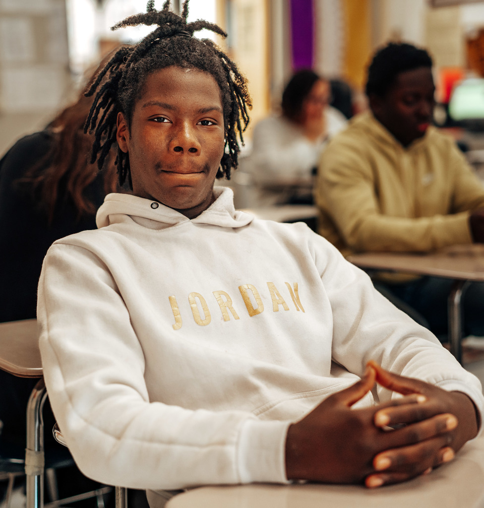 student sitting at his desk with his hands together looking at the camera. 
